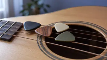 Illustrasjon av gitarplekter i ulike tykkelser på strengene til en akustisk gitar.